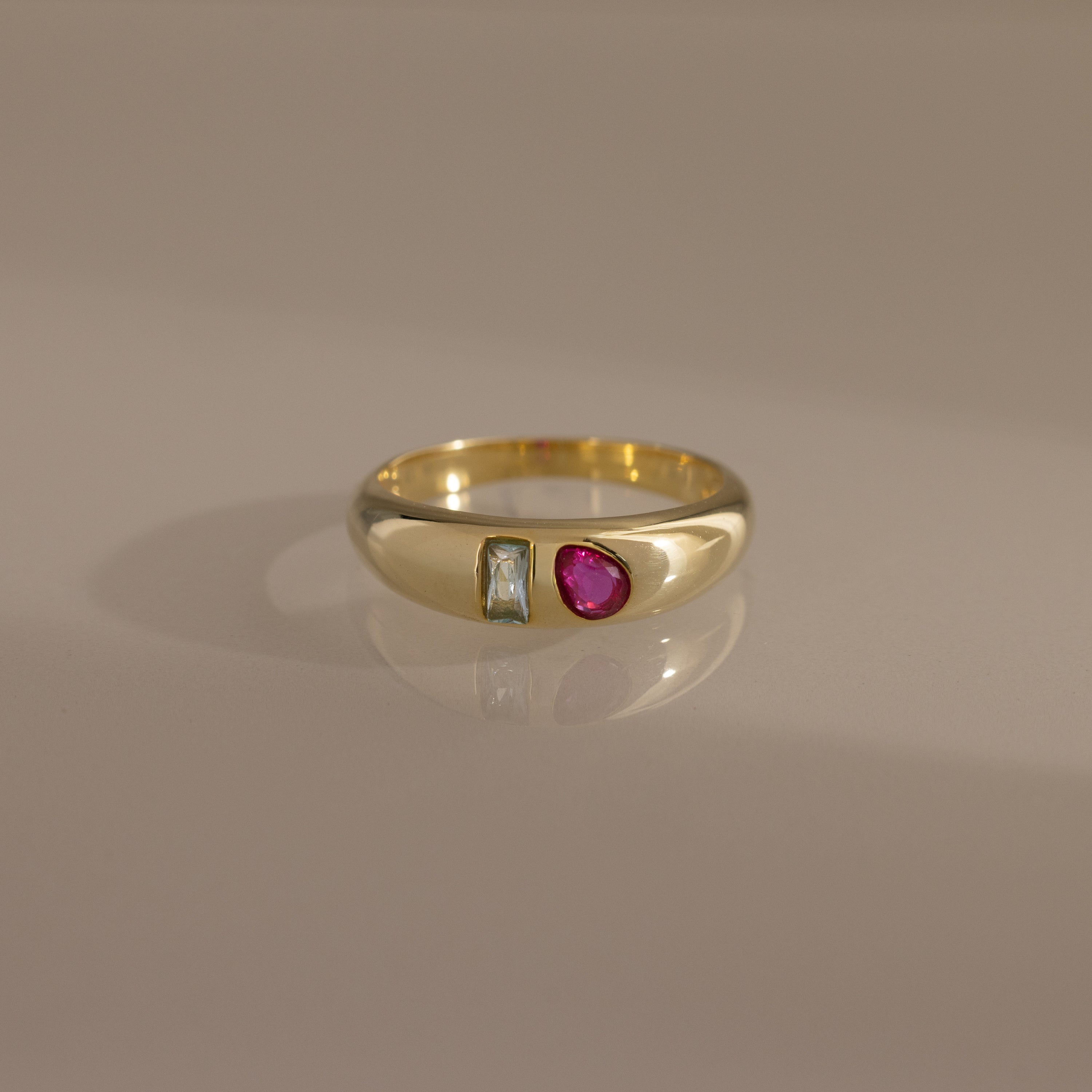 The Toi et Moi Dome Ring features a rectangular clear stone and a round red stone set side by side, creating a bold birthstone-inspired look.