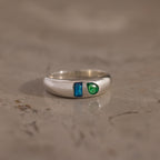 The Toi et Moi Dome Ring showcases a blue rectangular stone and a round green stone on a sleek silver dome band, elegantly displayed on marble.