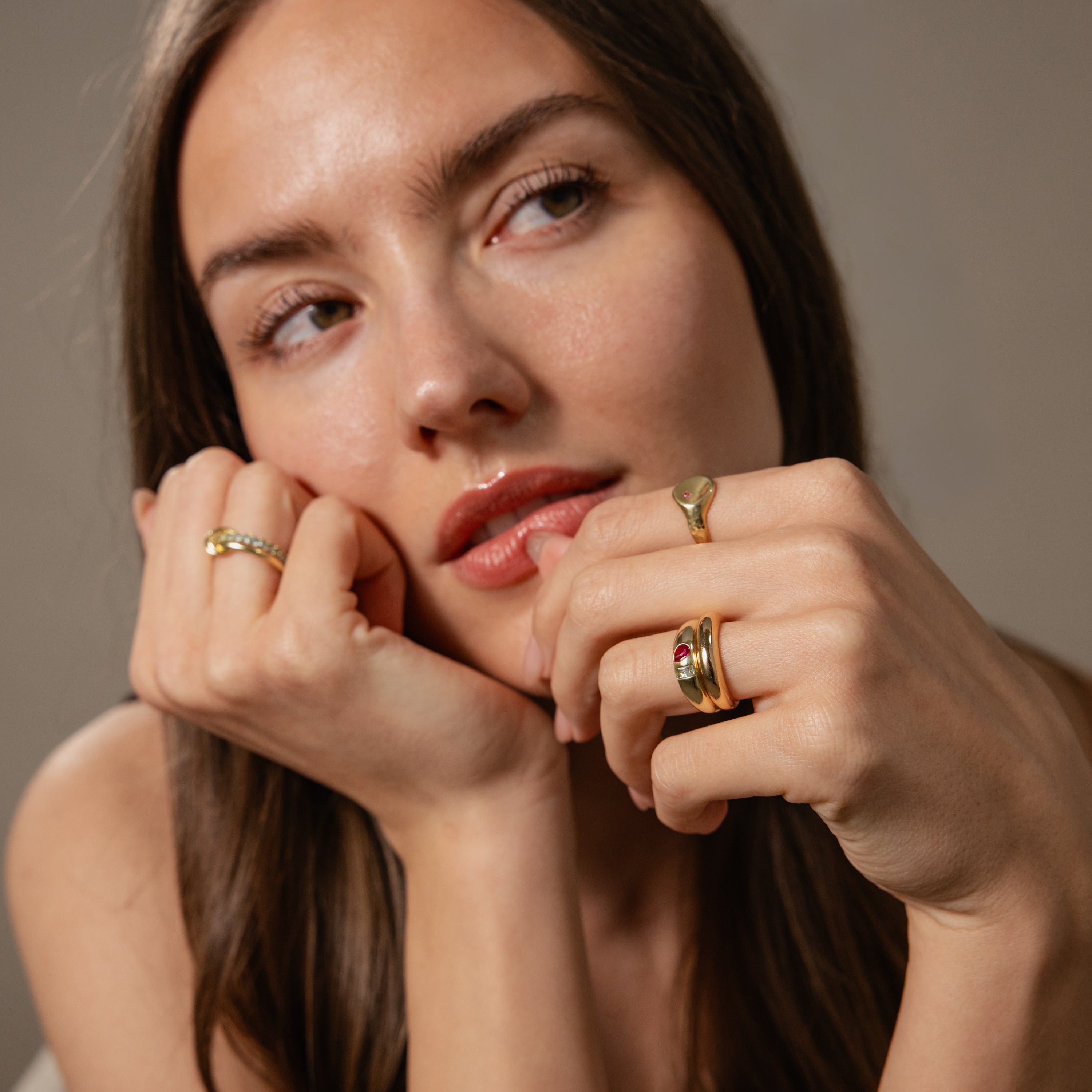 A woman with long brown hair rests her face on her hands, looking to the side while wearing the Toi et Moi Dome Ring.