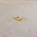 The Diamond Drop Curve Ring features a V-shaped gold band with a small central diamond, displayed on a textured light surface.