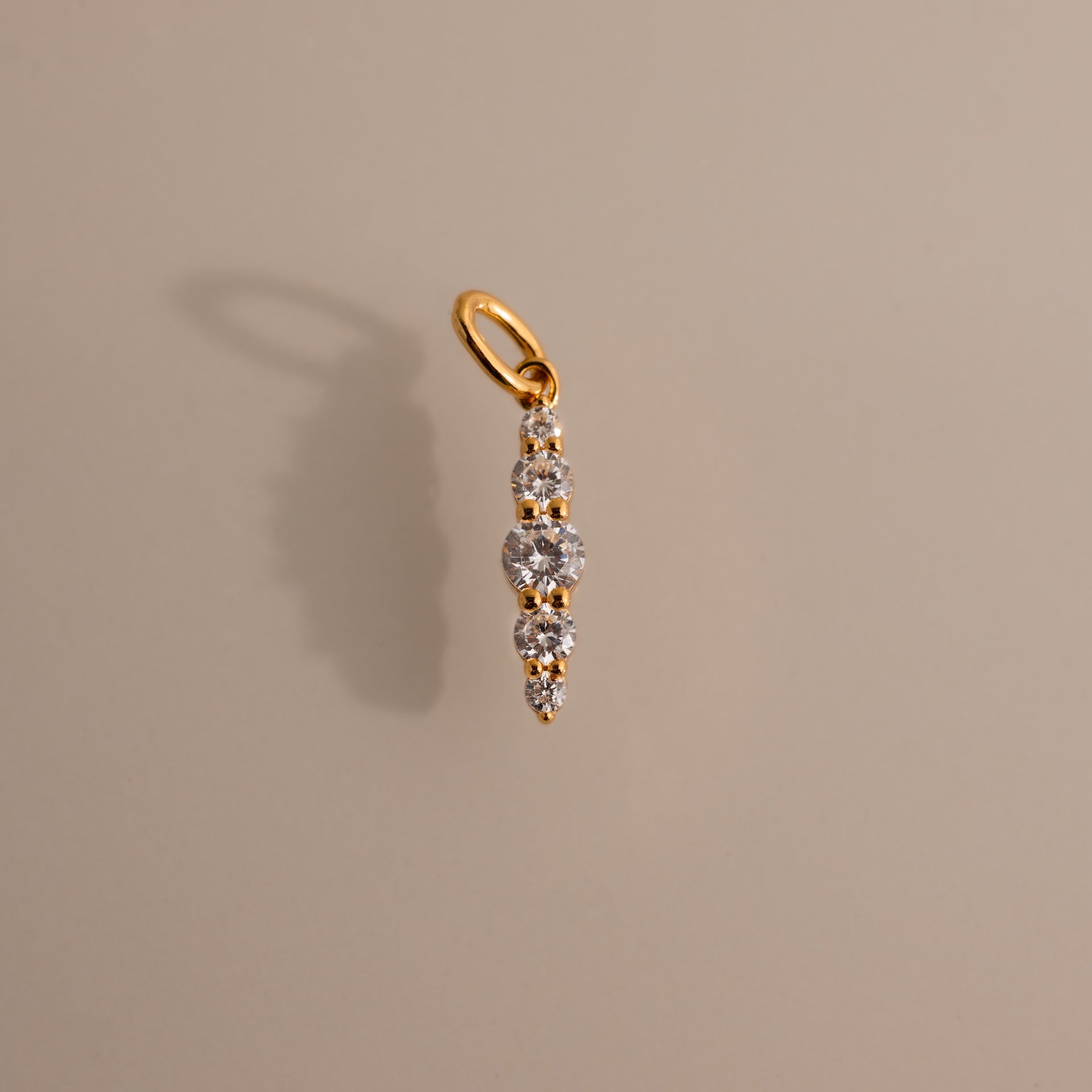 The Ombre Lace Diamond Charm features five vertically graduated round diamonds and casts a shadow on beige—a stunning gift for any birth month.