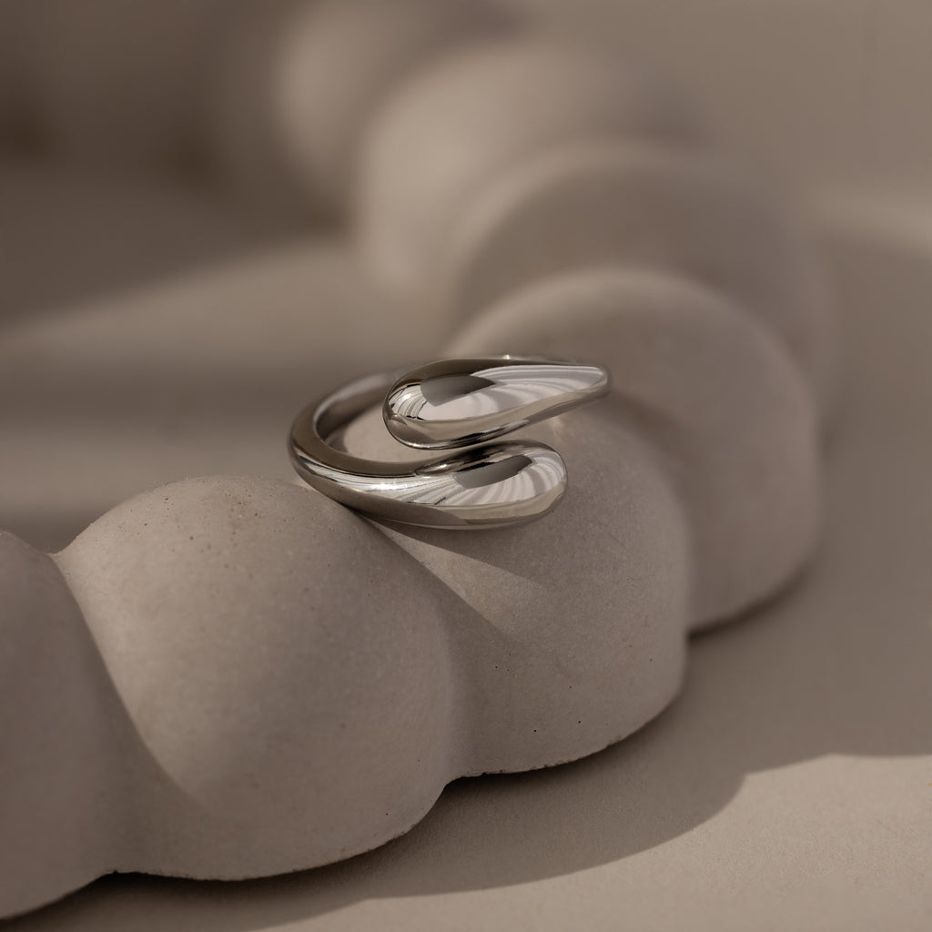 The Duo Dome Ring in White Gold, featuring a modern adjustable band, rests on a textured light beige sculptural surface, epitomizing contemporary sculptural jewelry.