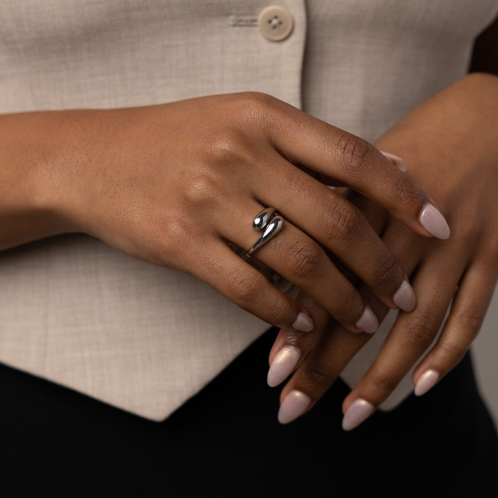 A hand with manicured nails wears the sculptural Duo Dome Ring in White Gold, its adjustable band gleaming in silver against a beige buttoned garment.