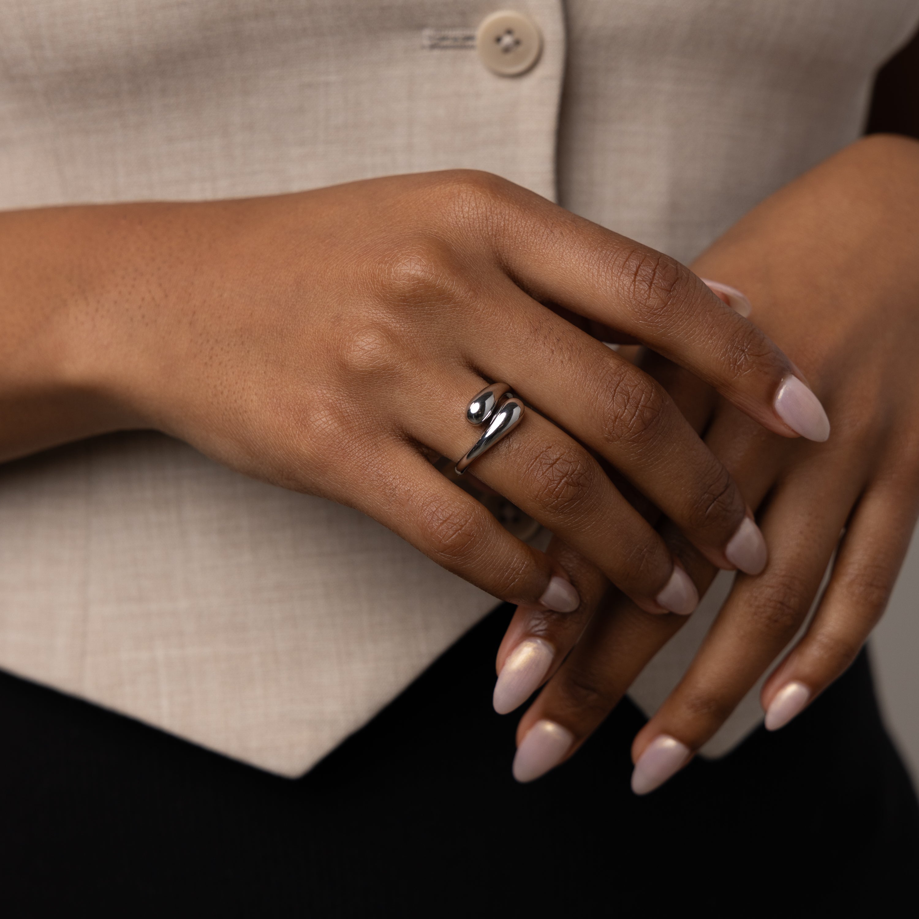 A hand with manicured nails wears the sculptural Duo Dome Ring in White Gold, its adjustable band gleaming in silver against a beige buttoned garment.