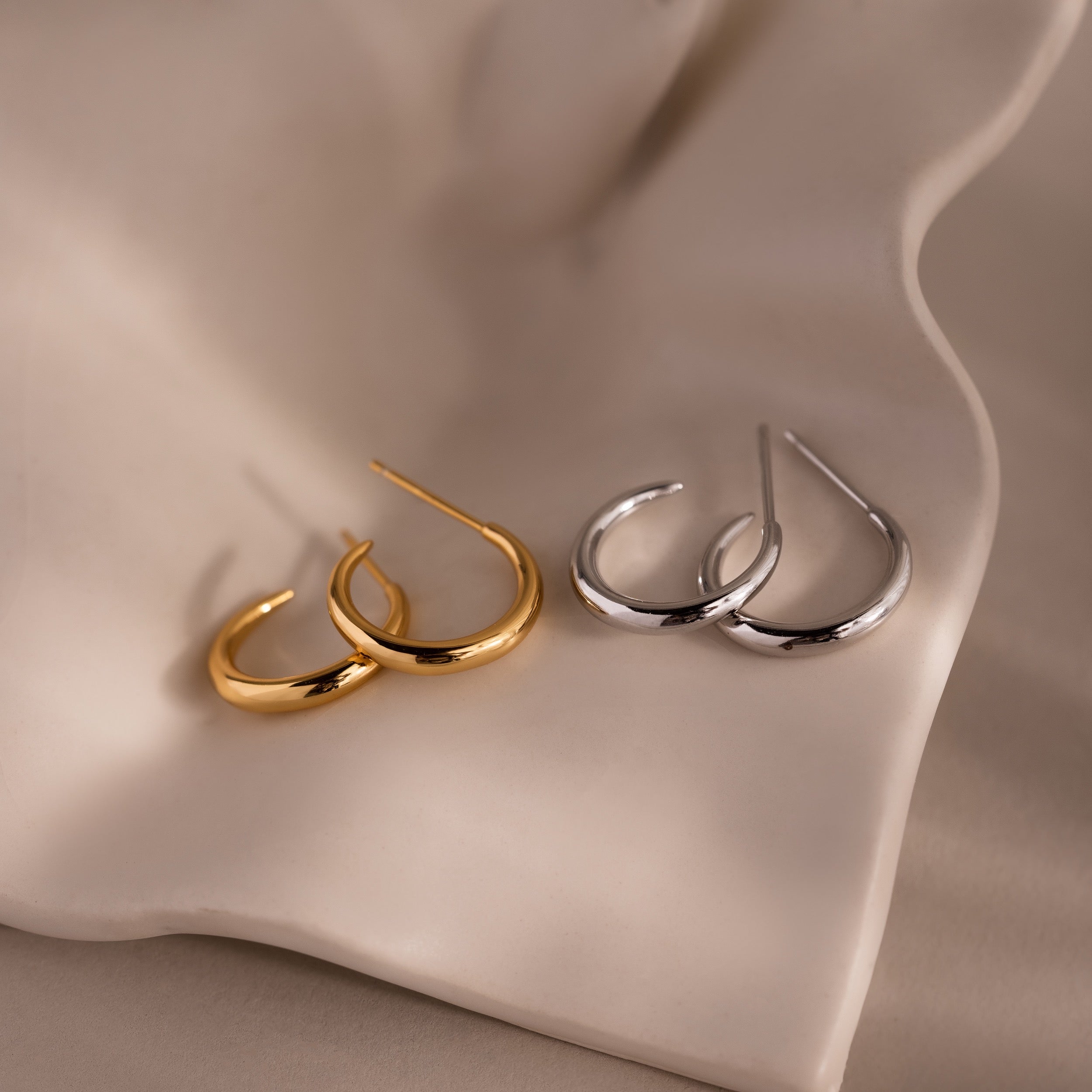 Gold and silver stud hoop earrings on a beige fabric background