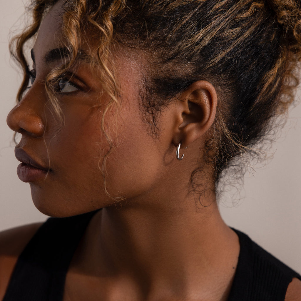 Close-up of a woman's profile with a silver stud hoop earring in a neutral background