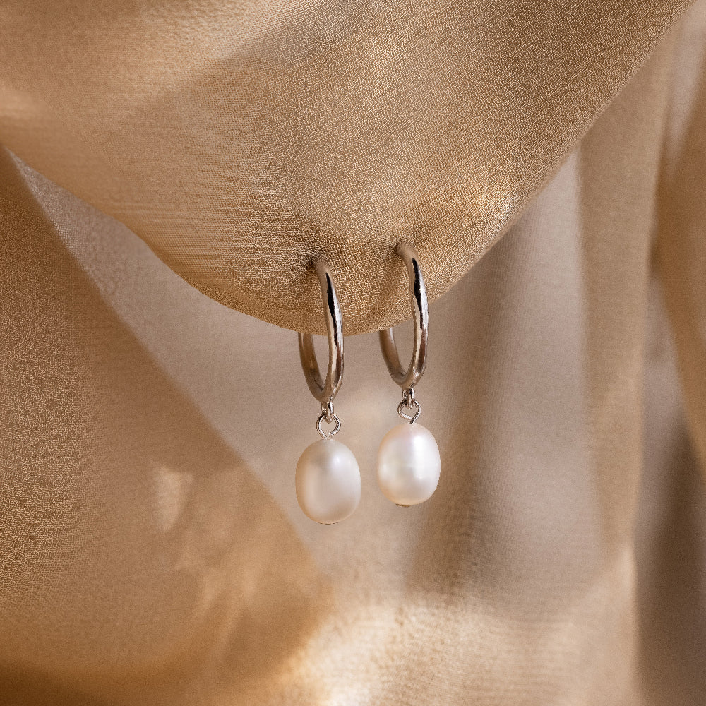 Pearl earrings hanging against a soft beige fabric background