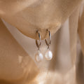 Pearl earrings hanging against a soft beige fabric background