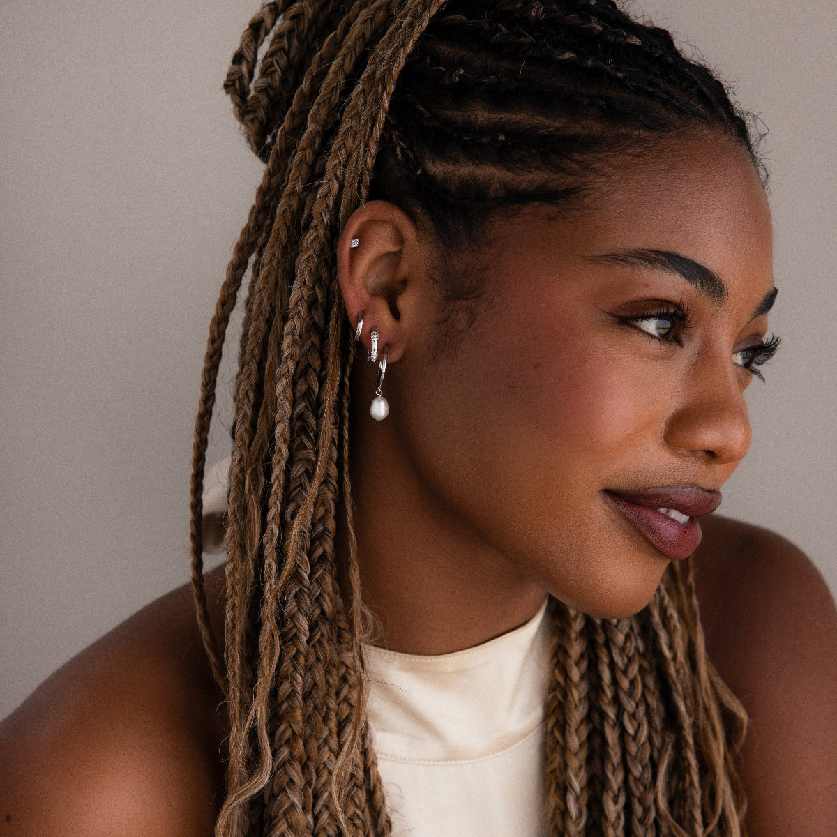 Woman with braided hair wearing multiple silver earrings against a neutral background