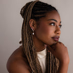 Woman with braided hair wearing a white top and various silver earrings against a neutral background