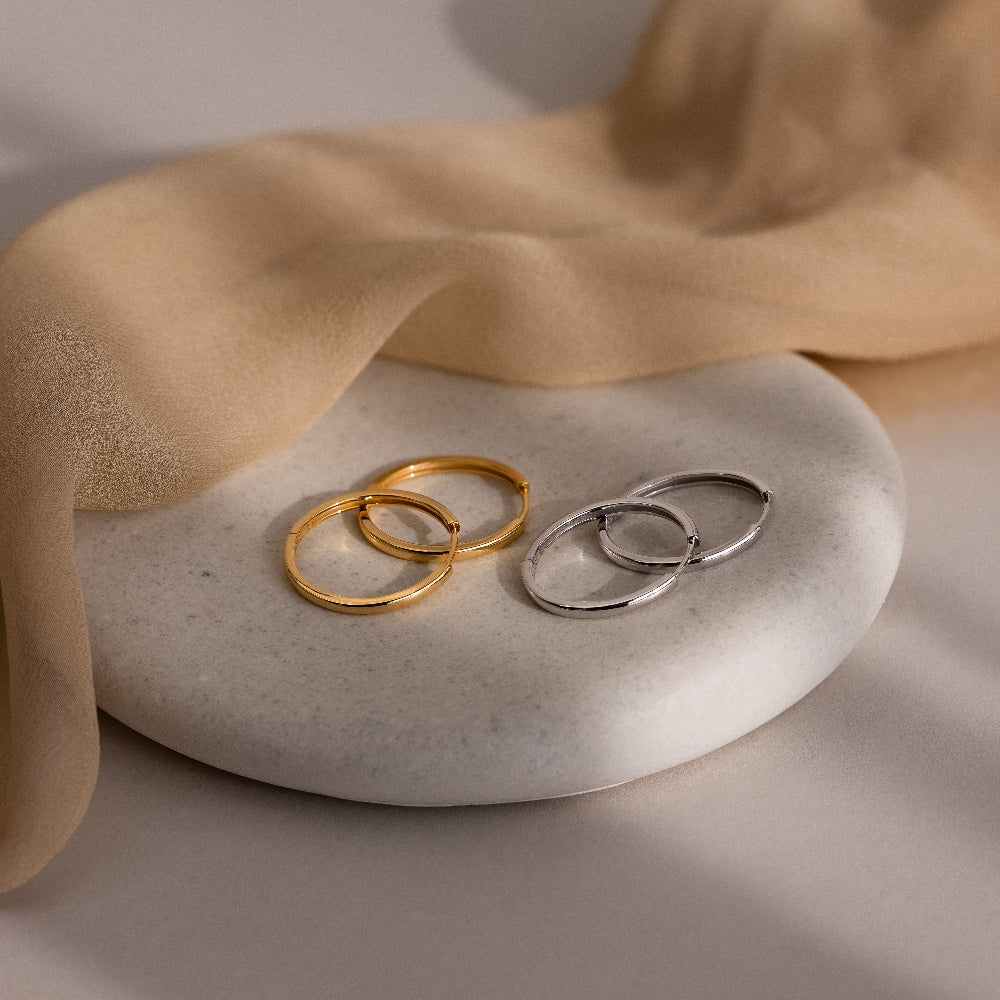 Two pairs of gold and silver hoop earrings on a stone surface with beige fabric.