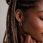 Close-up of a person wearing a silver hoop earring with braided hair.