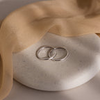 Two silver hoop earrings on a textured stone surface with beige fabric.