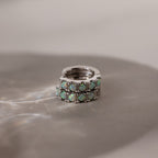 Silver huggie earrings with opal stones on a reflective surface