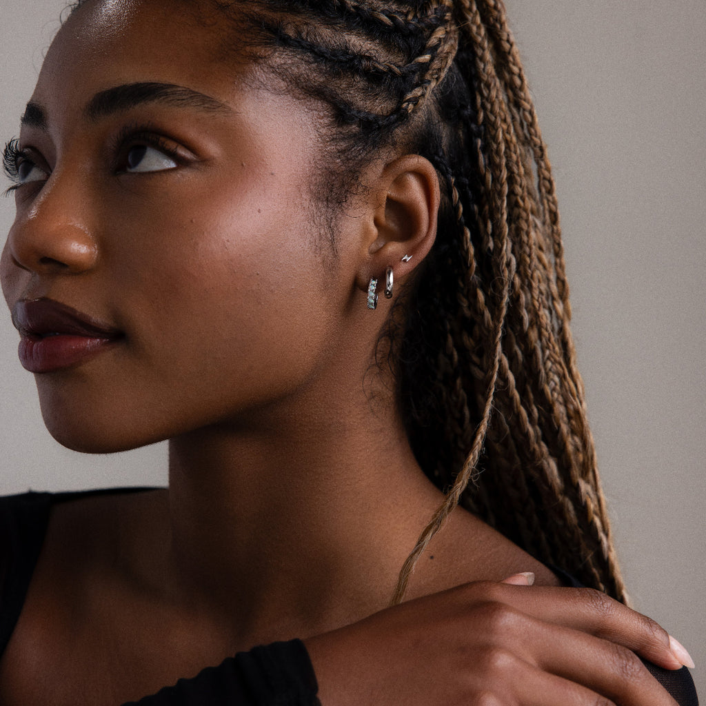 Woman with braided hair wearing various silver earrings against a neutral background