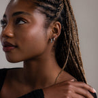 Woman with braided hair wearing various silver earrings against a neutral background