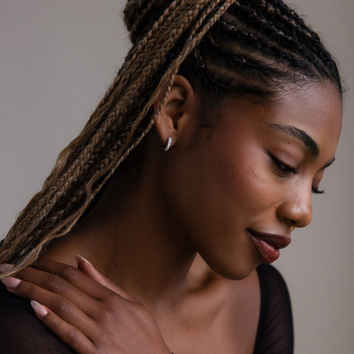 Woman with braided hair and opal hoop earrings wearing a dark top against a neutral background