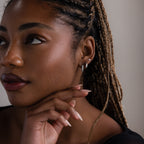 Close-up of a woman with braided hair, various silver earrings, and a neutral background