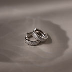Pair of silver hoop earrings with embedded stones on a beige fabric background