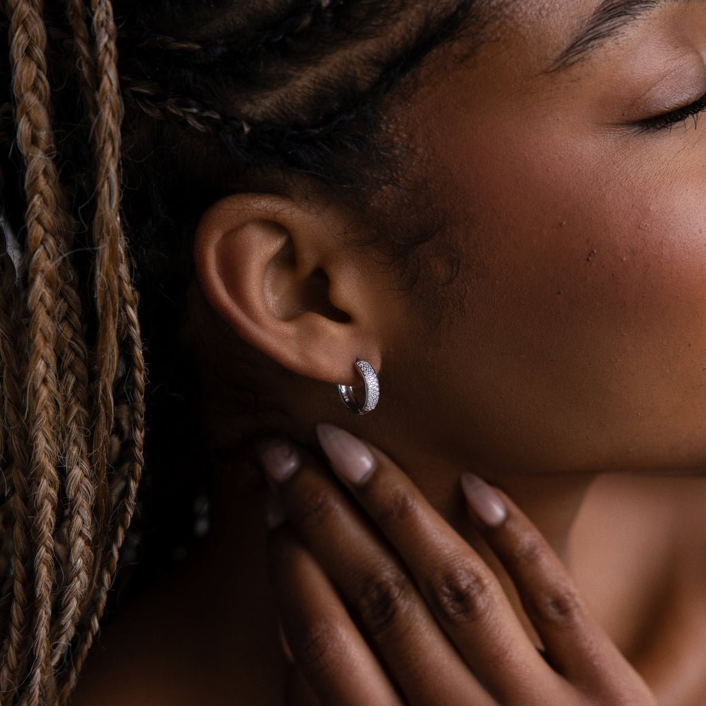 Close-up of a woman's ear with a pave diamond silver earring and hand near her face, with braided hair.
