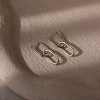 Pair of silver link hoop earrings on a textured beige surface