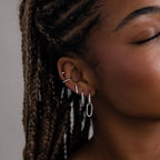 Close-up of a woman's ear with multiple silver earrings against a neutral background