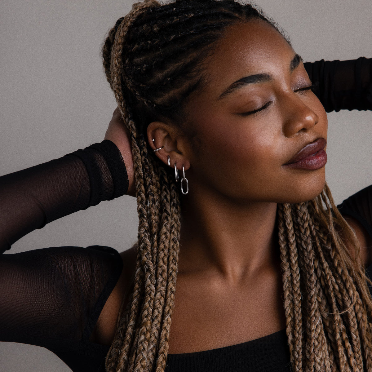 Woman with braided hair wearing silver earrings against a neutral background