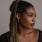 Woman with braided hair and silver link hoop earrings looking to the side against a neutral background