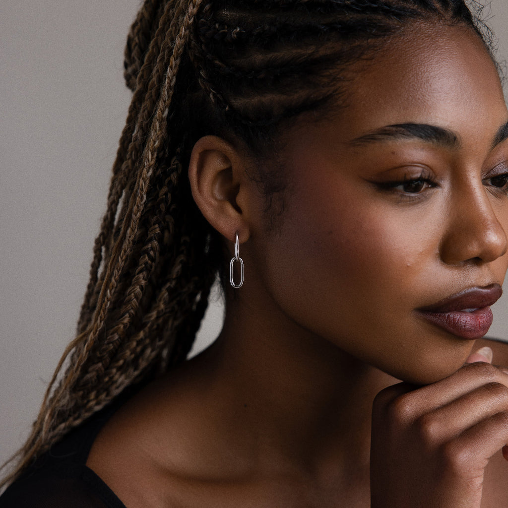 Woman with braided hair wearing a silver link hoop earring against a neutral background