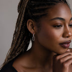Woman with braided hair wearing a silver link hoop earring against a neutral background