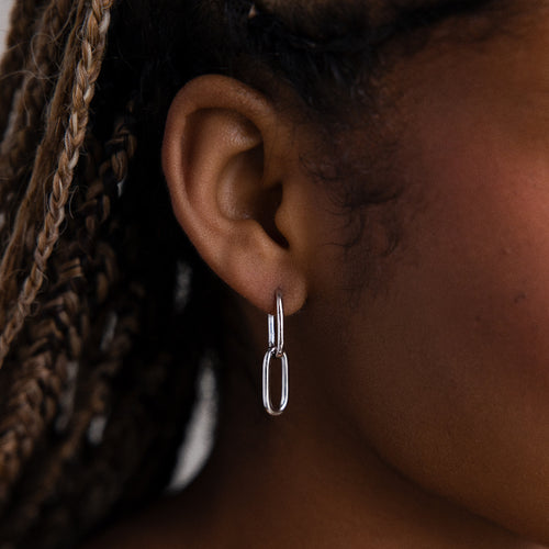 Close-up of an ear wearing a silver chain link hoop earring with braided hair.