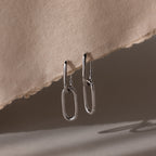 Silver linked hoop earrings on a textured beige surface