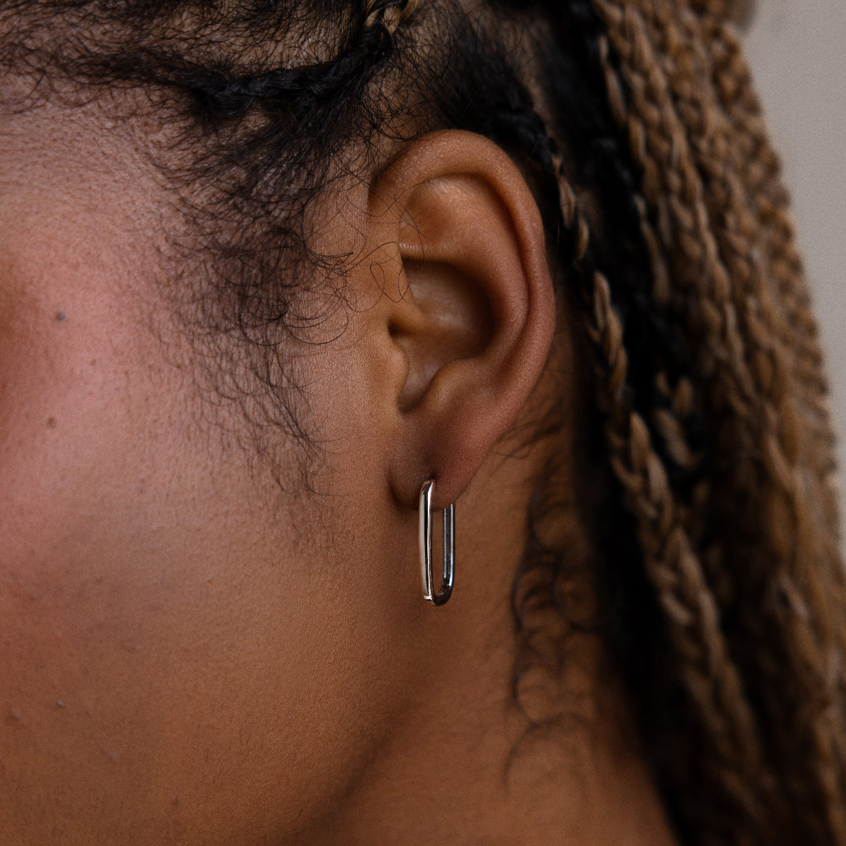 Close-up of a model wearing a silver rectangular hoop earring with braided hair.