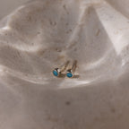 Pair of silver turquoise stud earrings on a textured beige surface