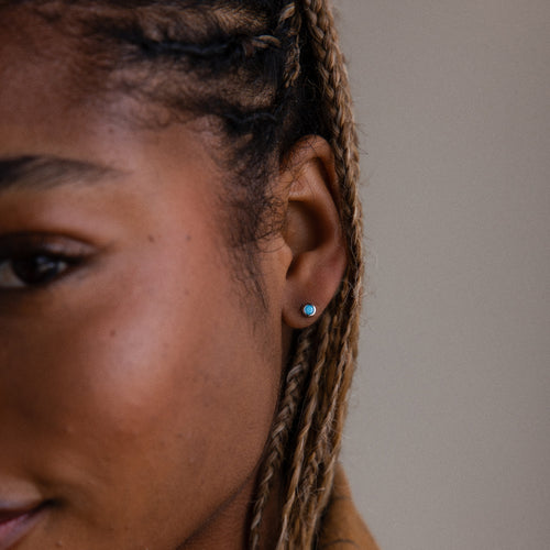 Close-up of a person with braided hair wearing a small turquoise stud earring.