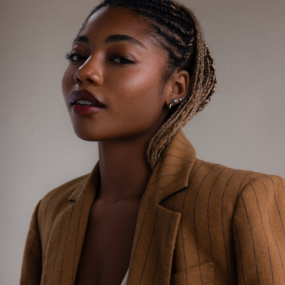 Woman wearing a brown pinstripe blazer against a neutral background with various silver turquoise stud earrings