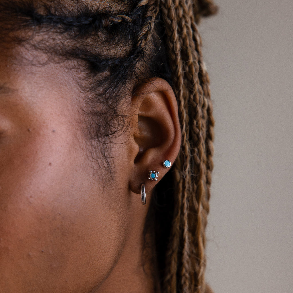 Close-up of an ear with various silver turquoise earrings against a neutral background