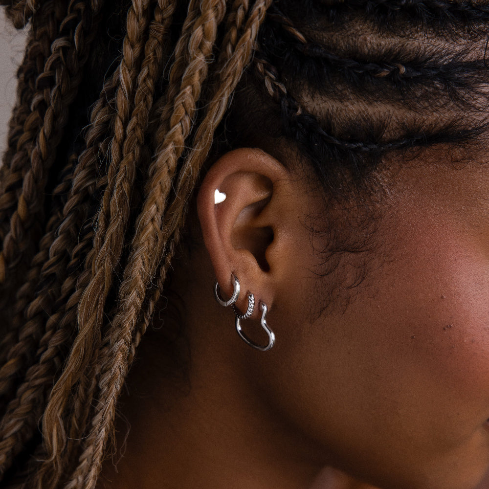Close-up of an ear with various silver hoop earrings and braided hair.