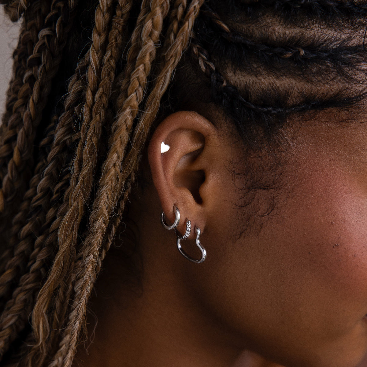 Close-up of a model with various silver hoop earrings and braided hair.