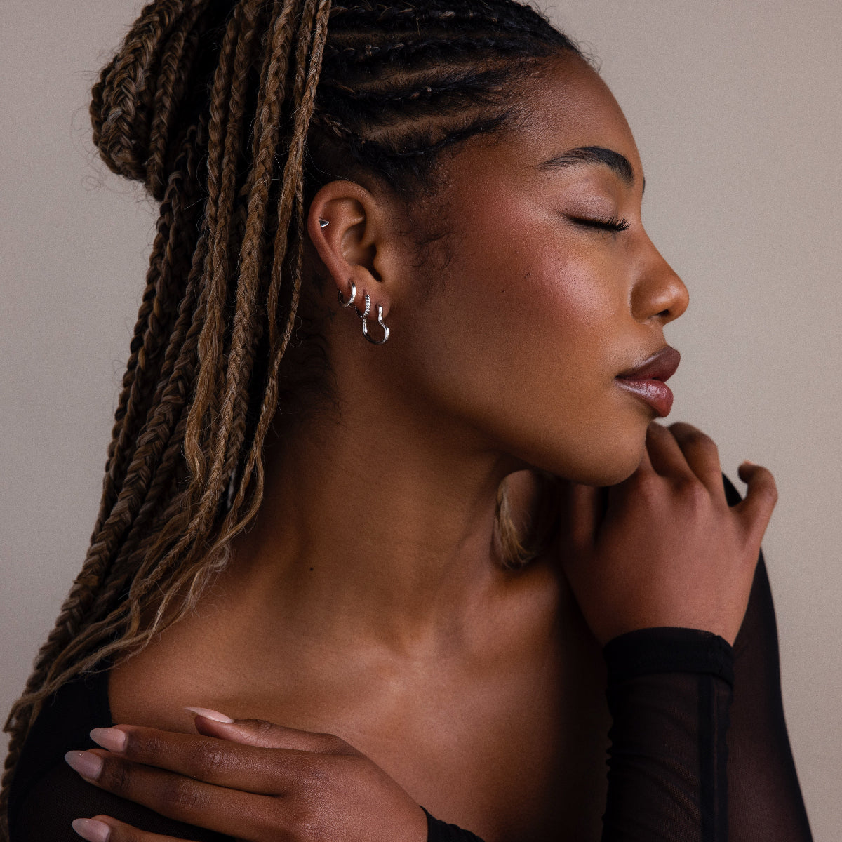 Woman with braided hair wearing silver earrings against a neutral background