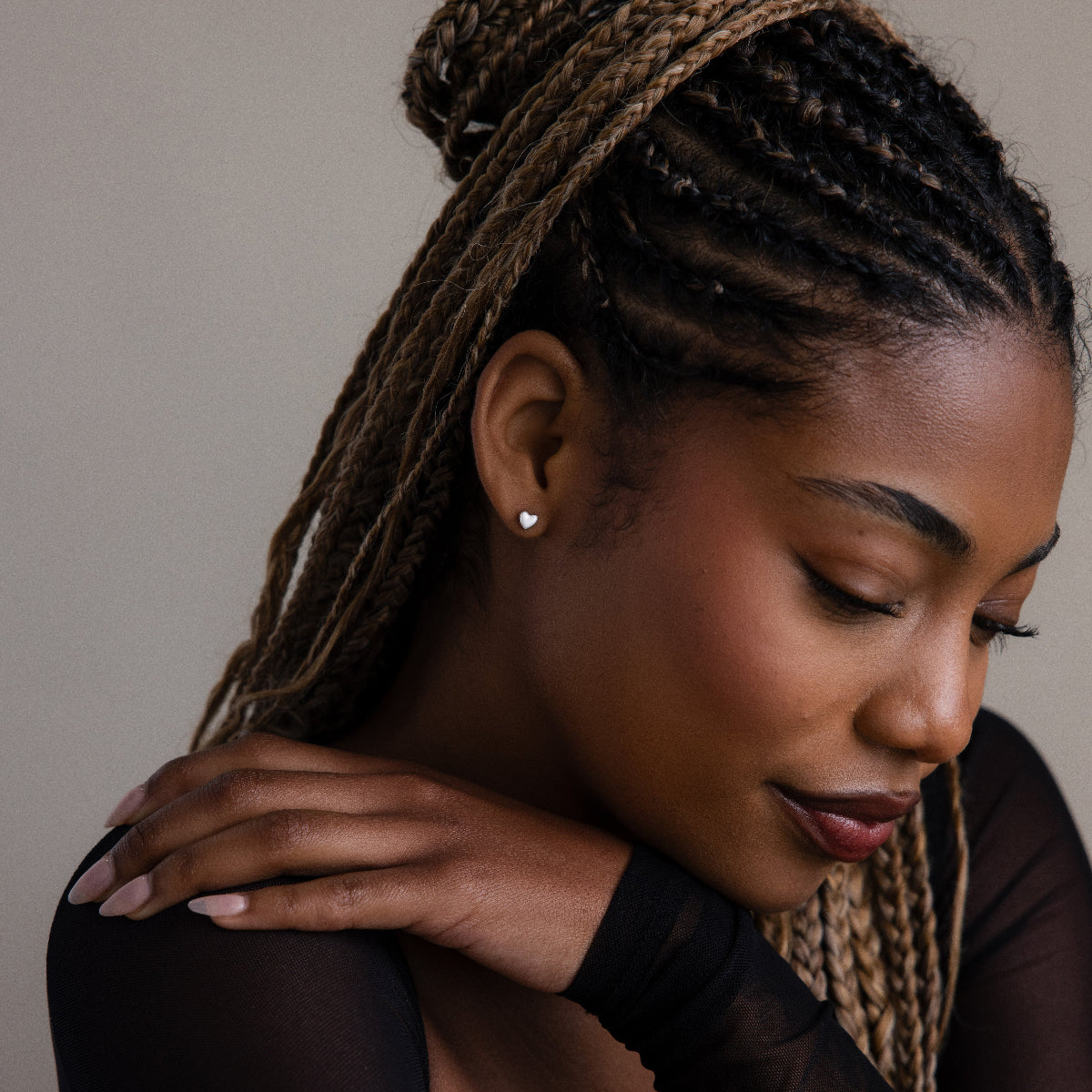 Woman with braided hair wearing a black top and a silver heart stud earring against a neutral background