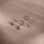 Silver floral rose shaped earrings on a beige surface