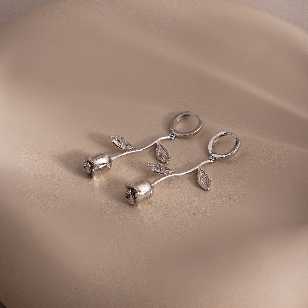 Silver floral rose shaped earrings on a beige surface