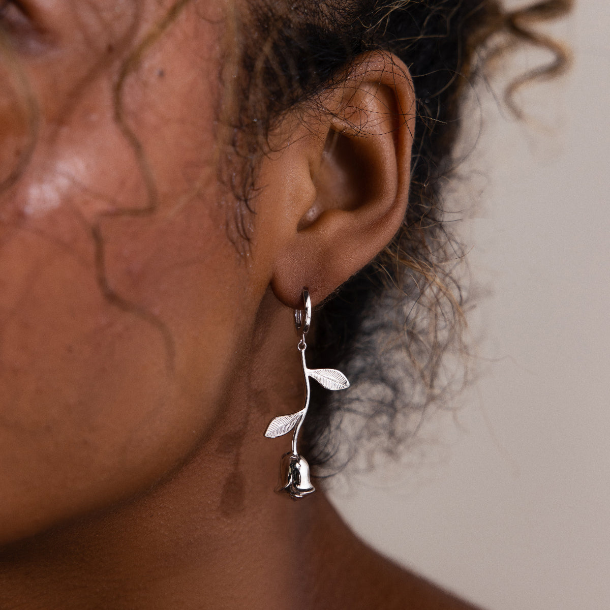 Silver floral rose earring worn by a woman with curly hair in a neutral background