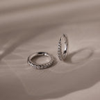 Pair of silver pave diamond hoop earrings on a beige fabric background