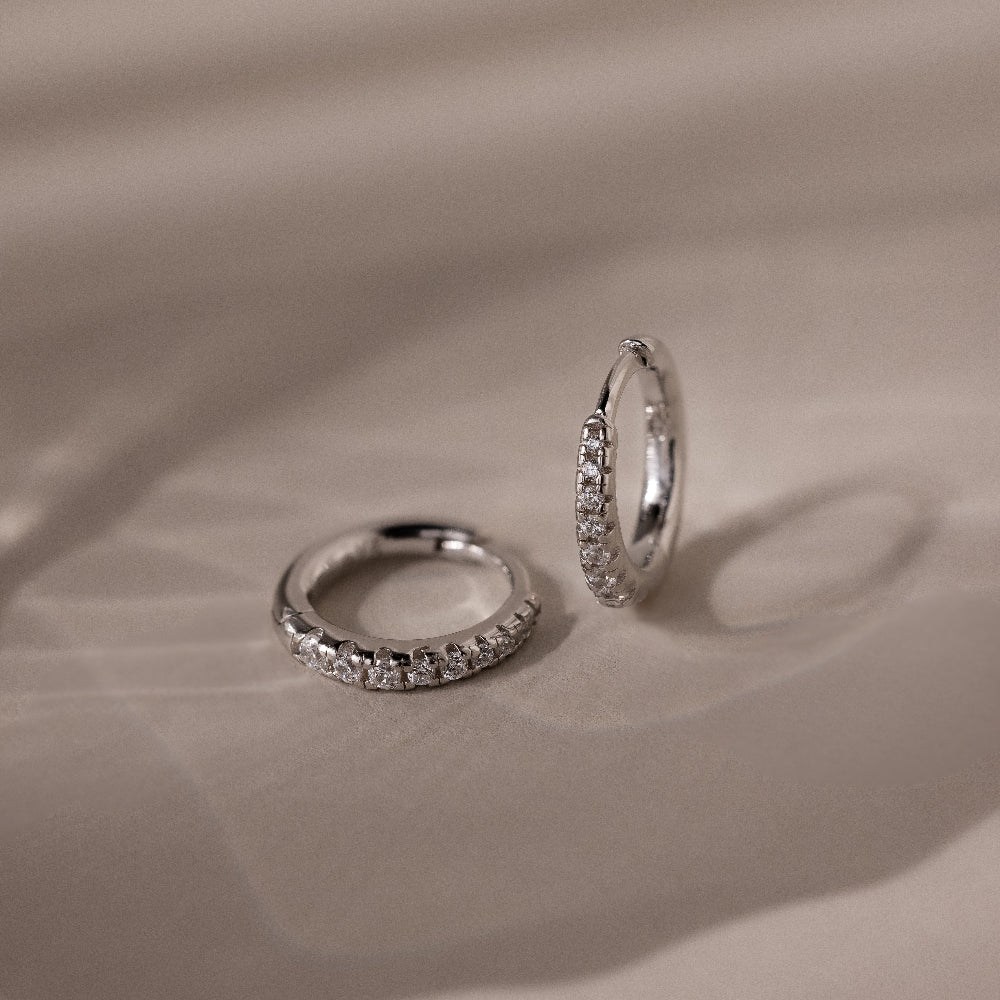Pair of silver pave diamond hoop earrings on a beige fabric background