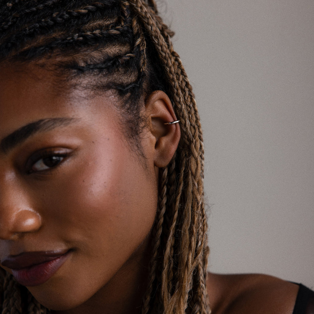 Close-up of a woman with braided hair and a silver cuff earring in a neutral background