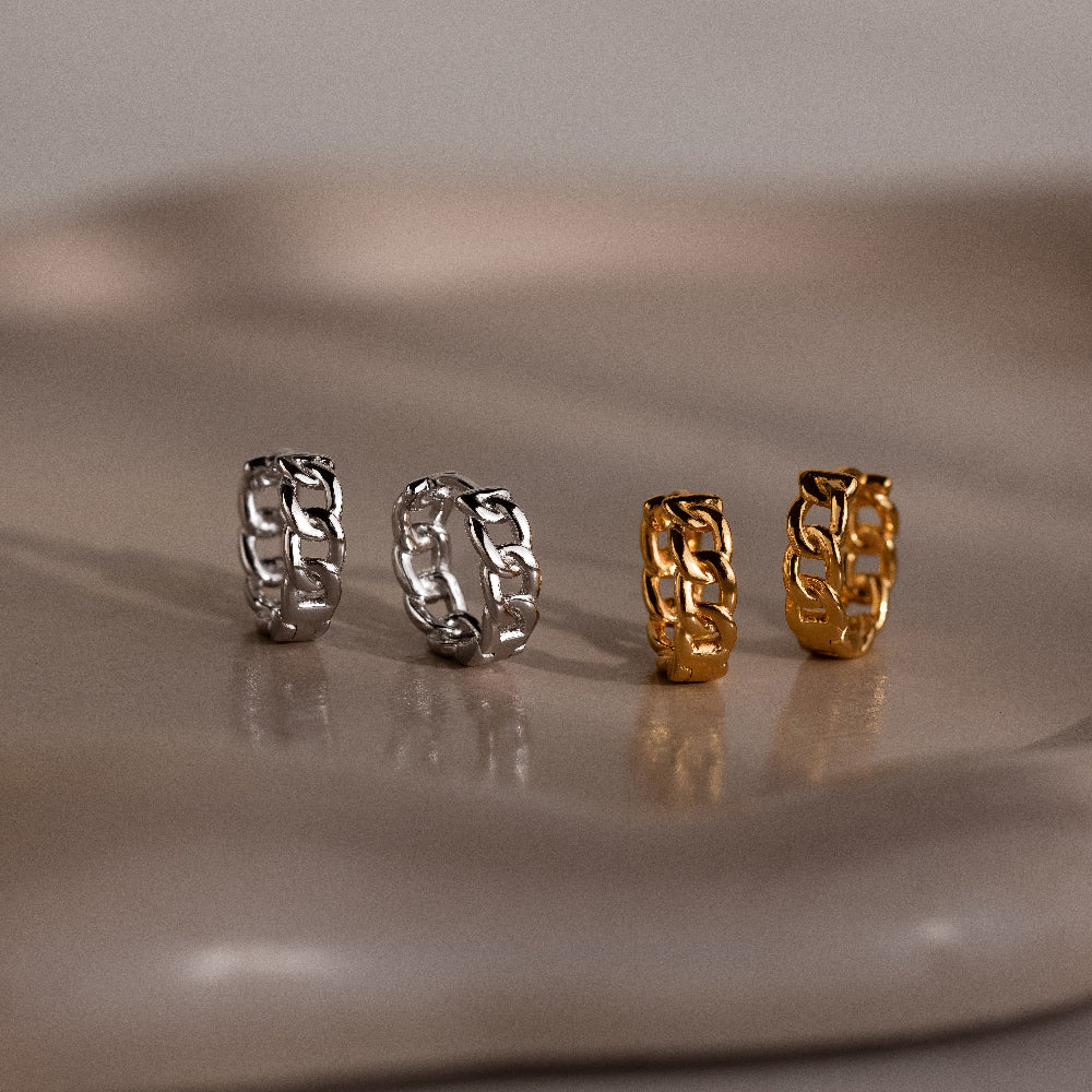 Four chain-link earrings in silver and gold on a reflective surface.
