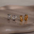 Four chain-link earrings in silver and gold on a reflective surface.