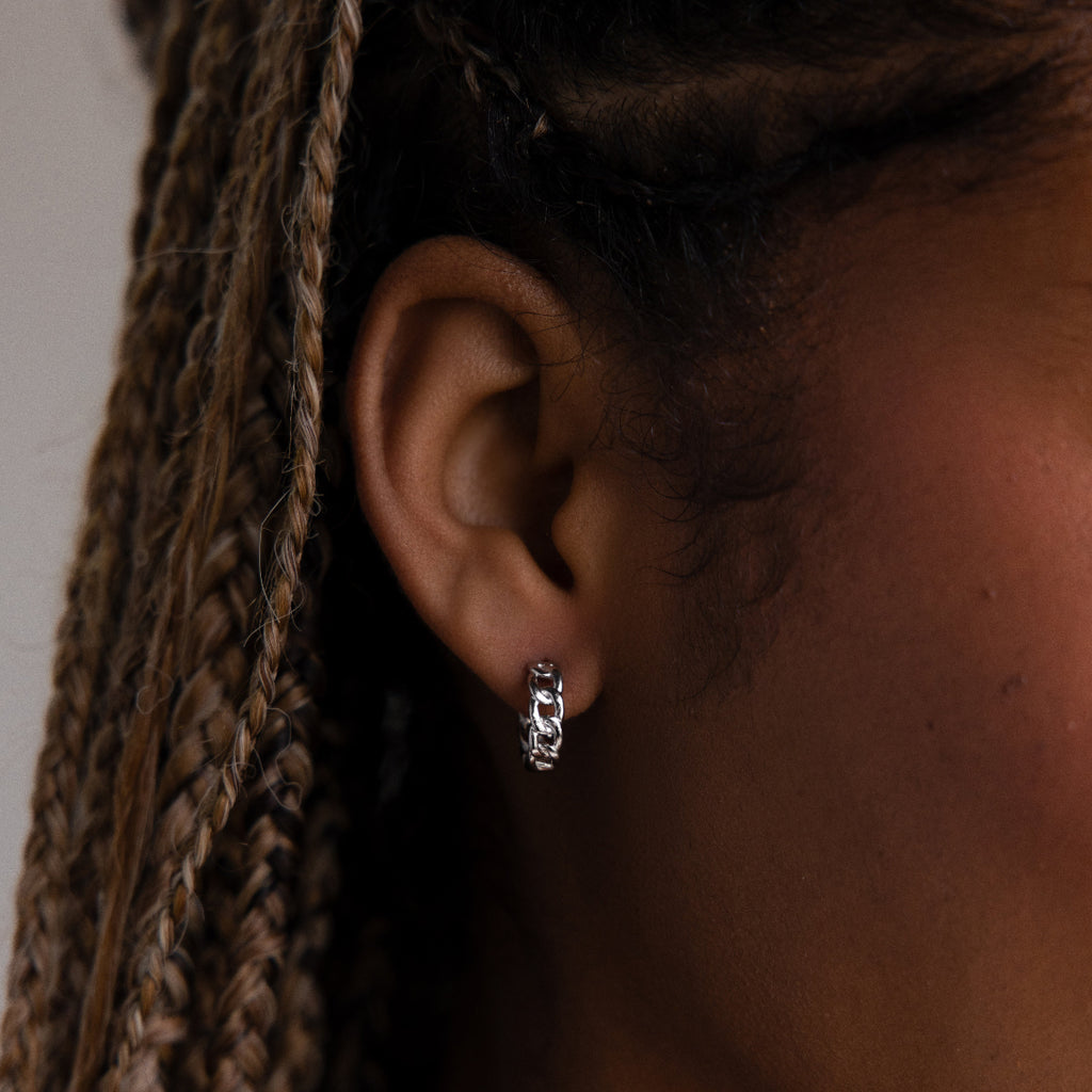 Close-up of a woman wearing a silver chain hoop earring with braided hair.